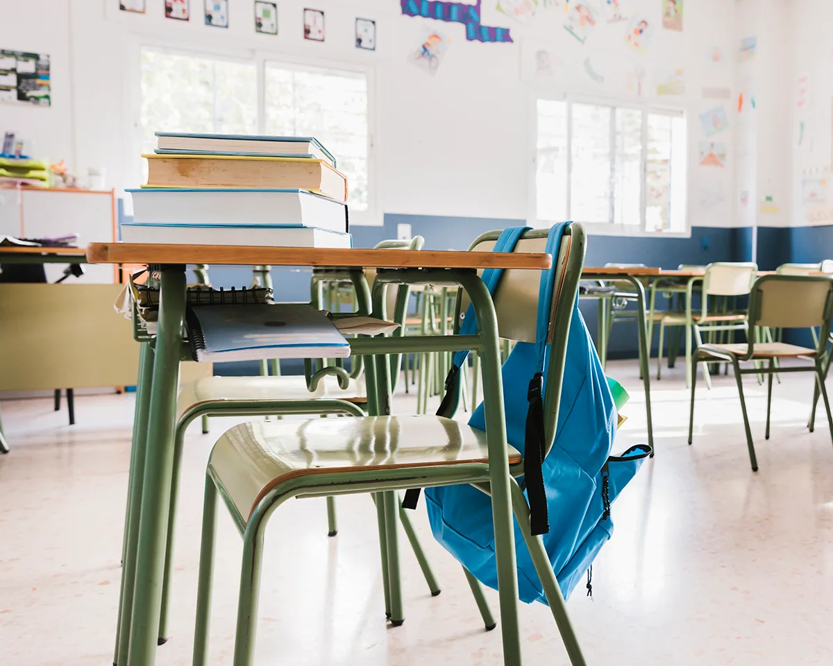 interior de una clase con pupitres carteras y libros